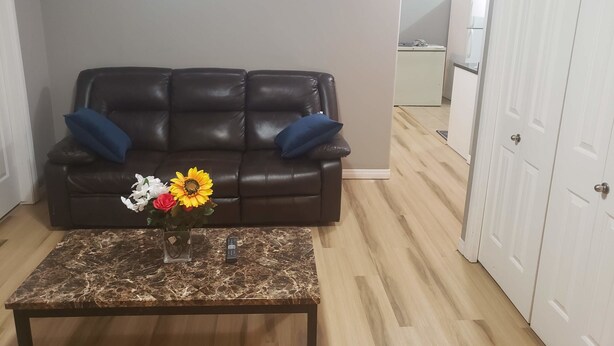 A living room with a brown leather sofa, two blue cushions, a marble coffee table with a vase of flowers, and a white door.