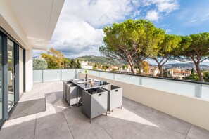 A balcony with a table and chairs, a view of a cityscape, and a tree. - L'Elégance (Nice)