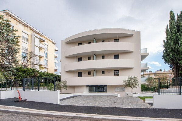 A multi-story building with a curved facade, a gated entrance, and a small landscaped area with trees. - L'Elégance (Nice)