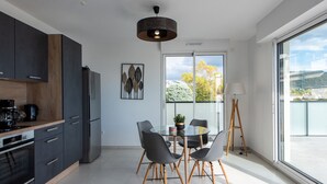 Et moderne køkken med mørke skabe, et rustfrit stål køleskab og et spiseområde med et glasbord og stole.