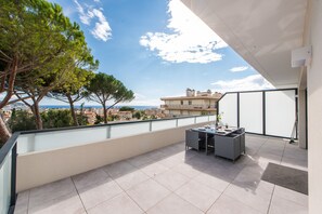 A balcony with a table and chairs, overlooking a cityscape and trees. - L'Elégance (Nice)