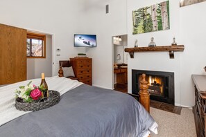 A bedroom with a bed, a fireplace, a television, and a wooden dresser.