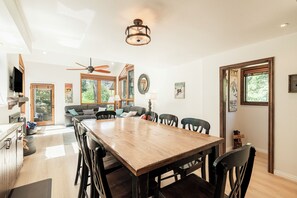 A spacious dining area with a wooden table and chairs, a ceiling fan, and a television in the background.