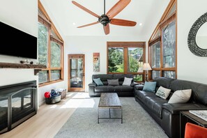A spacious living room with a fireplace, a large black leather sofa, a wooden coffee table, and a ceiling fan. - Stunning Views, Year-Round Recreation & Luxury Amenities at Park City Red Pine Townhouse! (Park City)