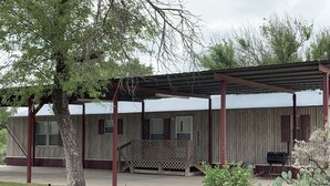 A rustic cabin with a covered porch, a small patio, and a grill area.