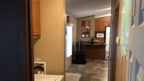 A narrow hallway with a laundry area on the left, a kitchen area with wooden cabinets and a microwave in the center, and a refrigerator on the right.