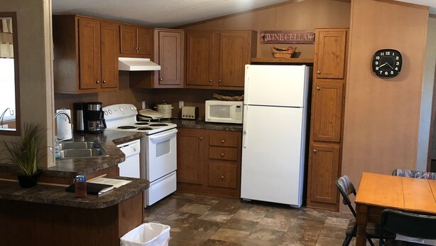 A compact kitchen with wooden cabinets, a white refrigerator, a microwave, and a stove. There's a clock on the wall and a small trash bin.