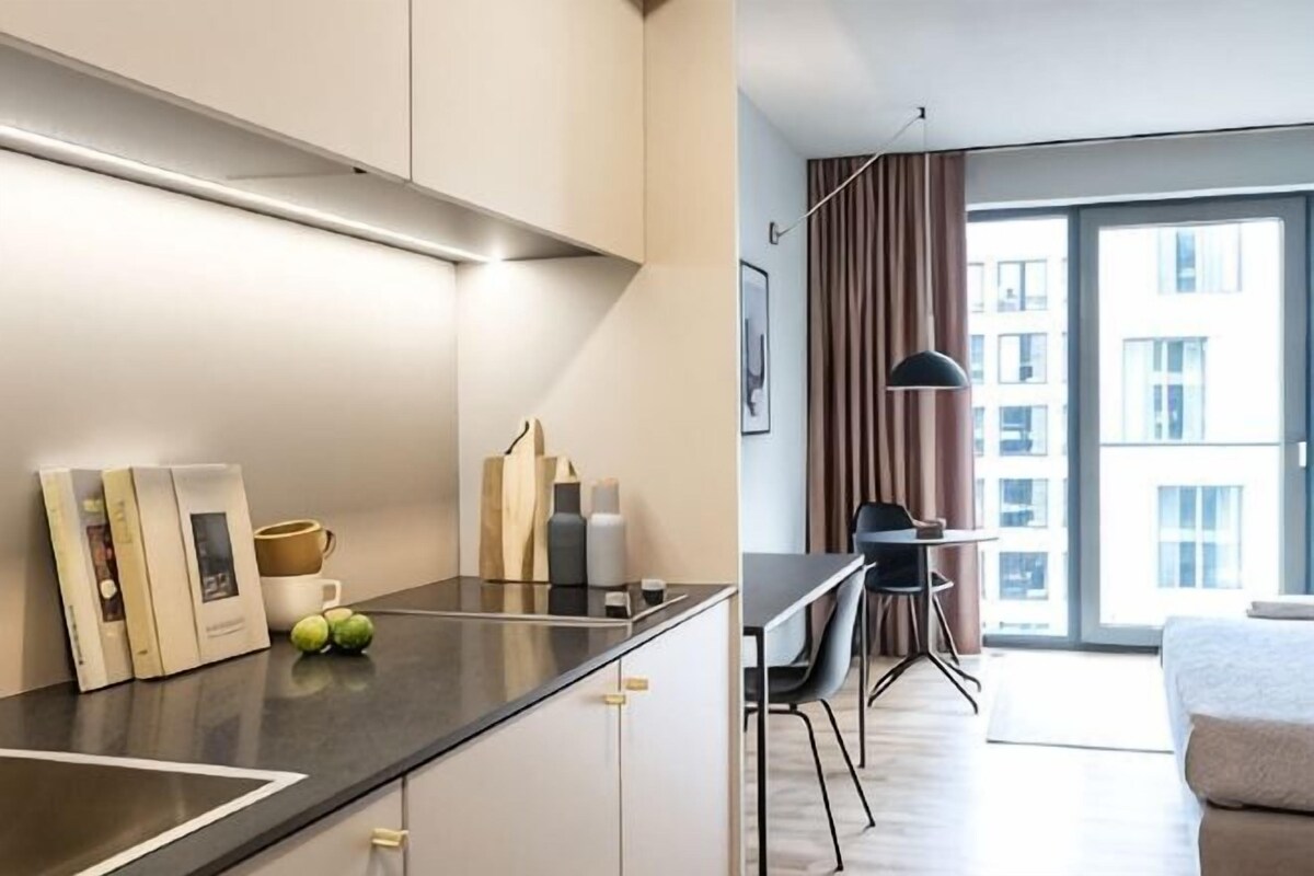 Een moderne hotelkamer met een keukenhoek, een eettafel en een groot raam met gordijnen.
