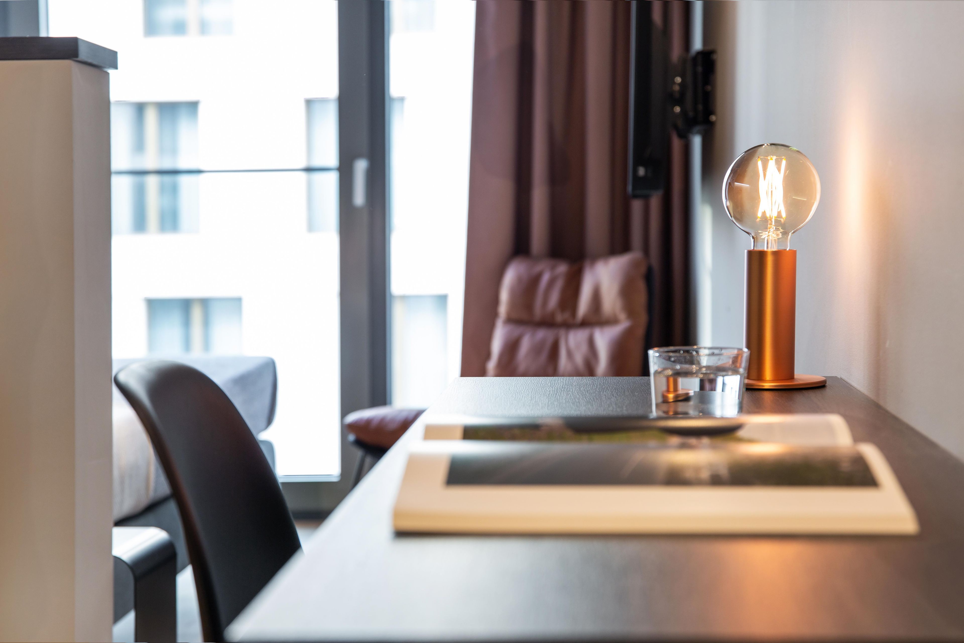 Una habitación de hotel con una mesa, una lámpara, un vaso y vistas al exterior.