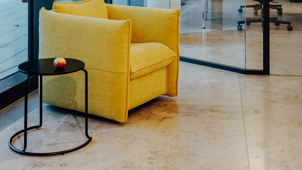 Een moderne kantoorruimte met een gele bank, een klein rond tafeltje met een appel en geometrische hanglampen.