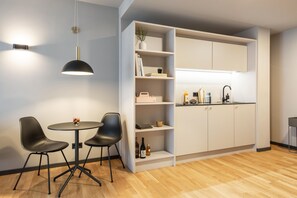 Une cuisine moderne avec des meubles blancs, un coin repas avec deux chaises noires et un luminaire suspendu.