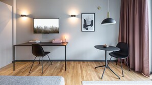 Ein modernes Zimmer mit Schreibtisch, zwei Stühlen, einem runden Tisch, einem wandmontierten Fernseher, einem Bilderrahmen mit abstraktem Gemälde und einer Pendelleuchte.