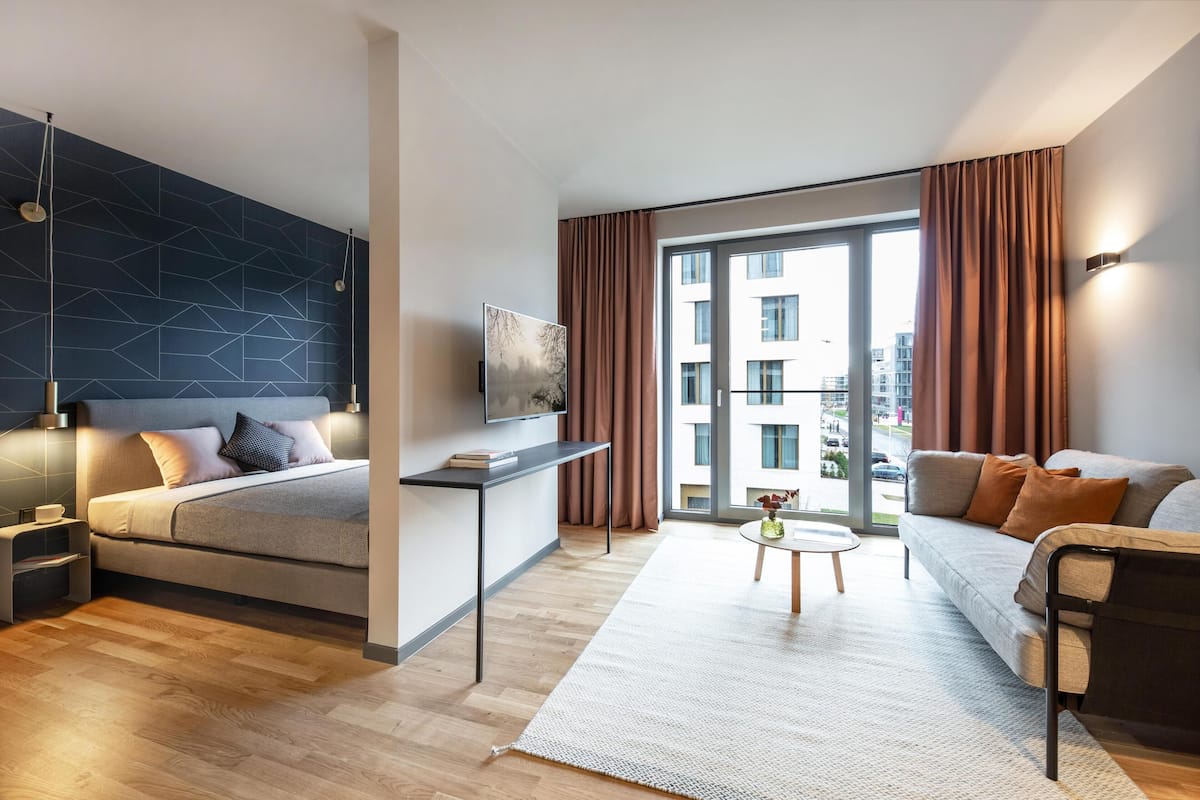 Une chambre d’hôtel moderne avec un lit, un canapé, une petite table et une grande fenêtre.