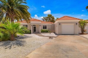 A two-story house with a red-tiled roof, a driveway, and a palm tree.