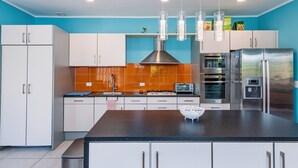 A modern kitchen with white cabinets, a central island, stainless steel appliances, and a blue accent wall. - Caribbean Oasis - 3 spacious suites, private pool (Noord)