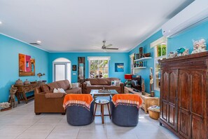 A spacious living room with a brown sofa set, two blue armchairs, and a wooden cabinet. - Caribbean Oasis - 3 spacious suites, private pool (Noord)
