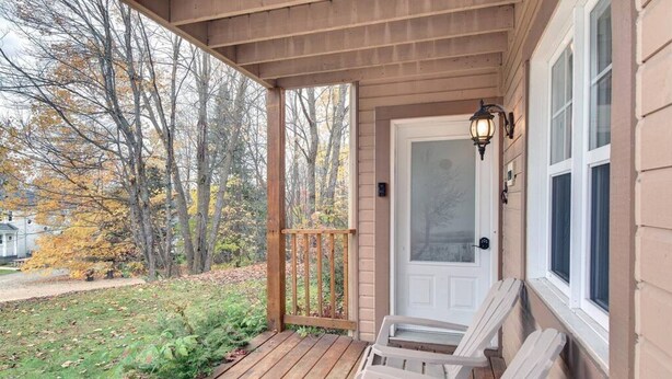 Eine hölzerne Veranda mit zwei weißen Adirondack-Stühlen, einer weißen Tür und einem Fenster mit einer Lampe.