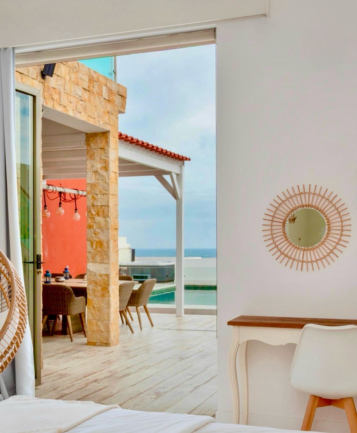 A modern room with a view of the ocean, a dining area with wicker furniture, and a unique wall decoration.