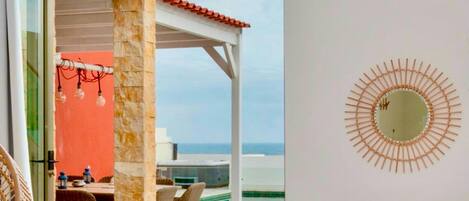 A modern room with a view of the ocean, a dining area with wicker furniture, and a unique wall decoration.