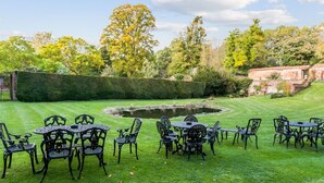 Un jardin avec un bassin, entouré d’une haie, et aménagé avec des tables et des chaises d’extérieur.
