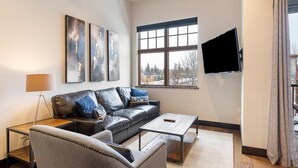 En moderne stue med en lædersofa, et sofabord, en gulvlampe og et fladskærms-TV monteret på væggen.