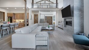 A spacious living area with a large L-shaped sectional sofa, a dining area with bar stools, a kitchen with wooden cabinets, and a fireplace. - Deschutes Executive Retreat - 6BR Luxury Rental (Deschutes County)