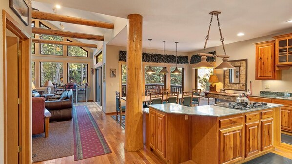 Kitchen features a stove, wooden cabinetry, and stone countertop, adjacent to a dining and seating area.