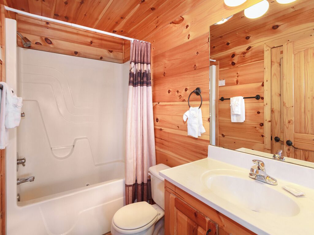 Une salle de bain rustique, avec une cabine en bois, une baignoire, des toilettes et un lavabo.
