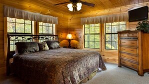 Ein Schlafzimmer in einer Holzhütte mit einem Bett, einem Schminktisch, einer Lampe und einem Deckenventilator.