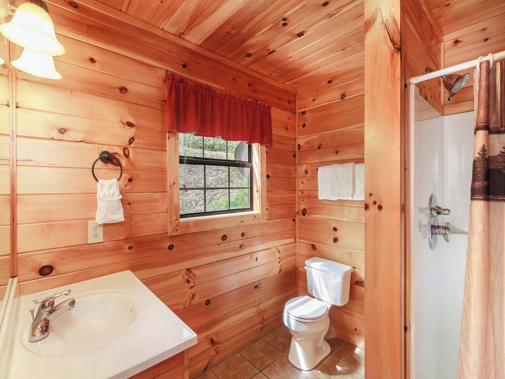 A wooden cabin bathroom with a sink, toilet, and window.