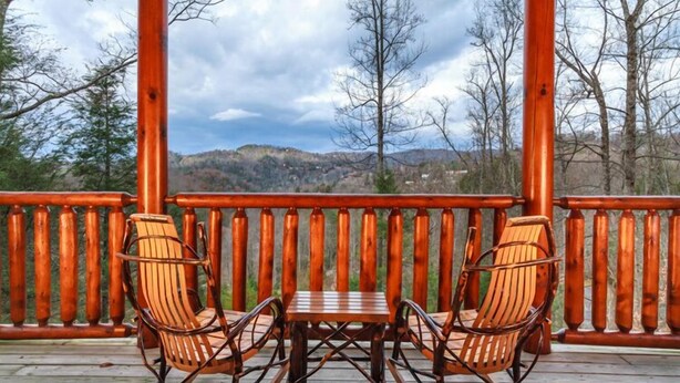 Eine Holzterrasse mit zwei Schaukelstühlen und einem kleinen Tisch, mit Blick auf eine gebirgige Landschaft.