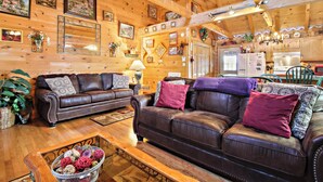 A cozy log cabin interior with two leather sofas, wooden flooring, and a kitchen area visible in the background. - Alpine Ski Lodge by Jackson Mountain Rentals (Gatlinburg)