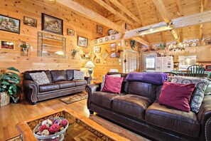 Un acogedor interior de cabaña de madera con dos sofás de cuero, piso de madera y una cocina visible al fondo.
