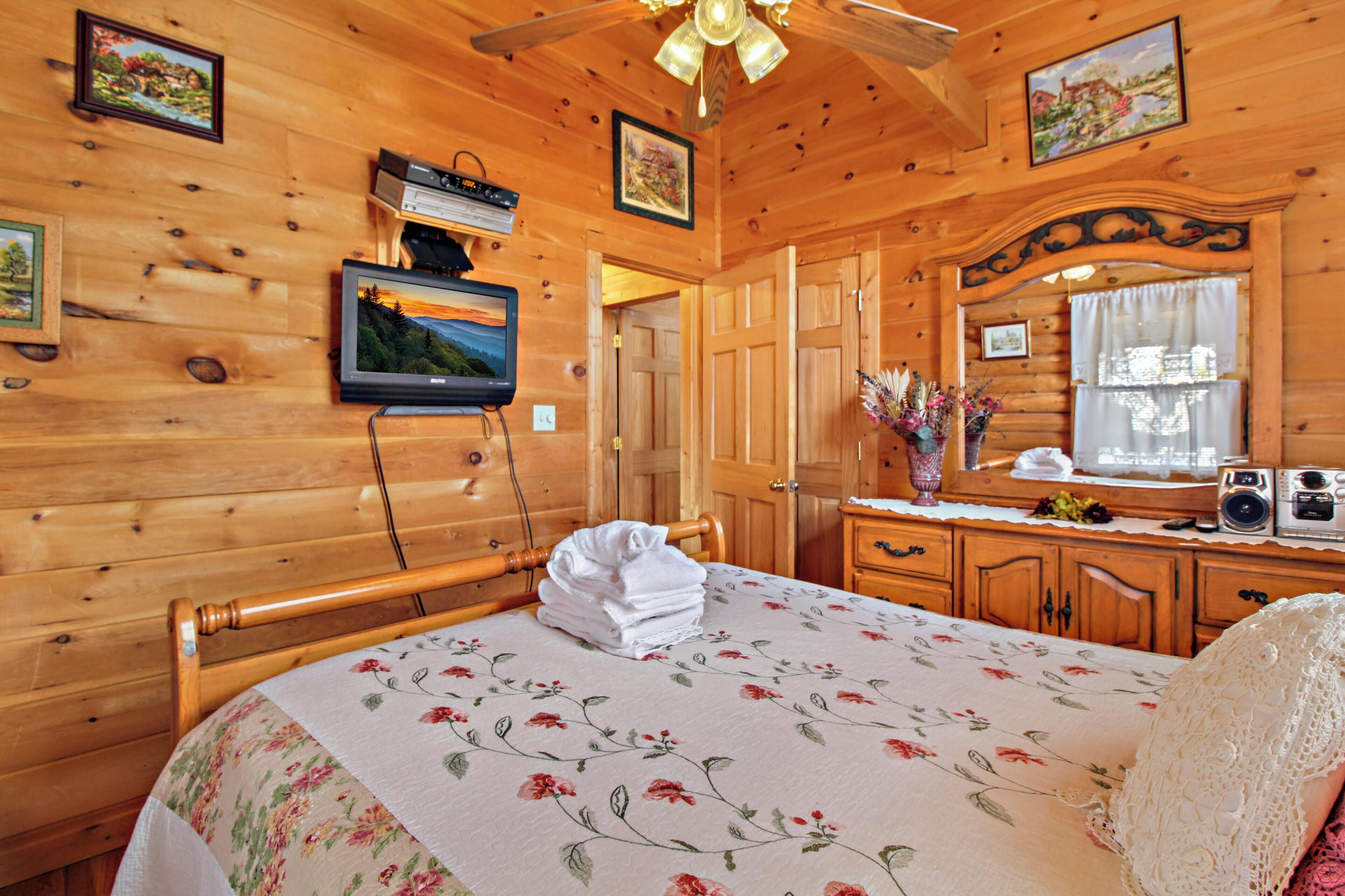 Une chambre dans une cabane en bois, avec un lit, une télévision, un bureau avec une radio et une fenêtre avec des rideaux.
