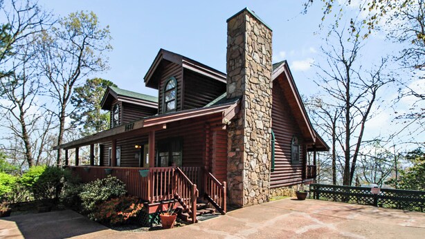 A log cabin with a stone chimney, a porch with a railing, and a view of trees. - Alpine Ski Lodge by Jackson Mountain Rentals (Gatlinburg)