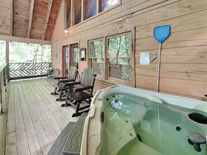 A wooden deck with outdoor seating, a hot tub, and windows overlooking a forested area.