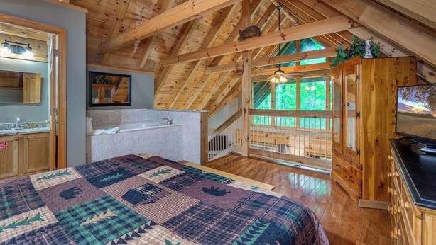 Un dormitorio acogedor en el ático con techo de madera, una cama grande, televisor integrado y vistas al exterior.