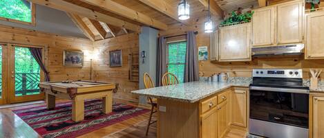 A wooden cabin interior with a pool table, kitchen area, and a dining table.