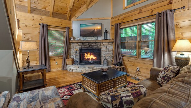 A cozy cabin interior with a stone fireplace, wooden walls, and a comfortable seating area. - Above Ole Smoky's Clouds by Jackson Mountain Rentals (Gatlinburg)