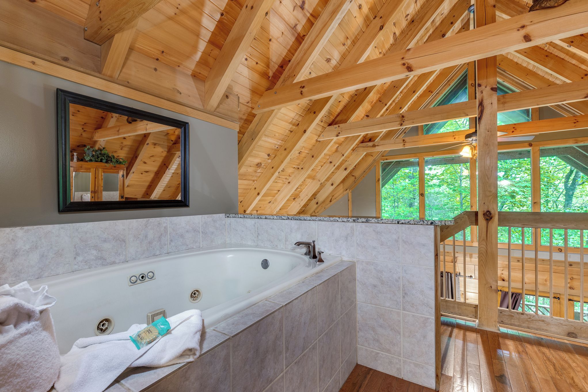 A wooden cabin interior with a large bathtub, a mirror, and a view of the outdoors.