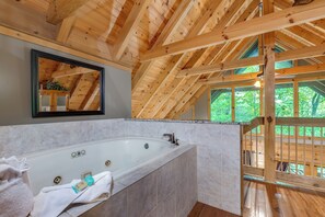 Ein Holzblockhaus-Innenraum mit einer großen Badewanne, einem Spiegel und Blick ins Freie.