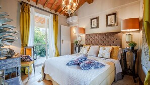 Une chambre à coucher avec un grand lit, deux lampes de chevet, un lustre et un balcon avec des rideaux jaunes.