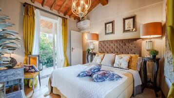 A bedroom with a large bed, two bedside lamps, a chandelier, and a balcony with yellow curtains.