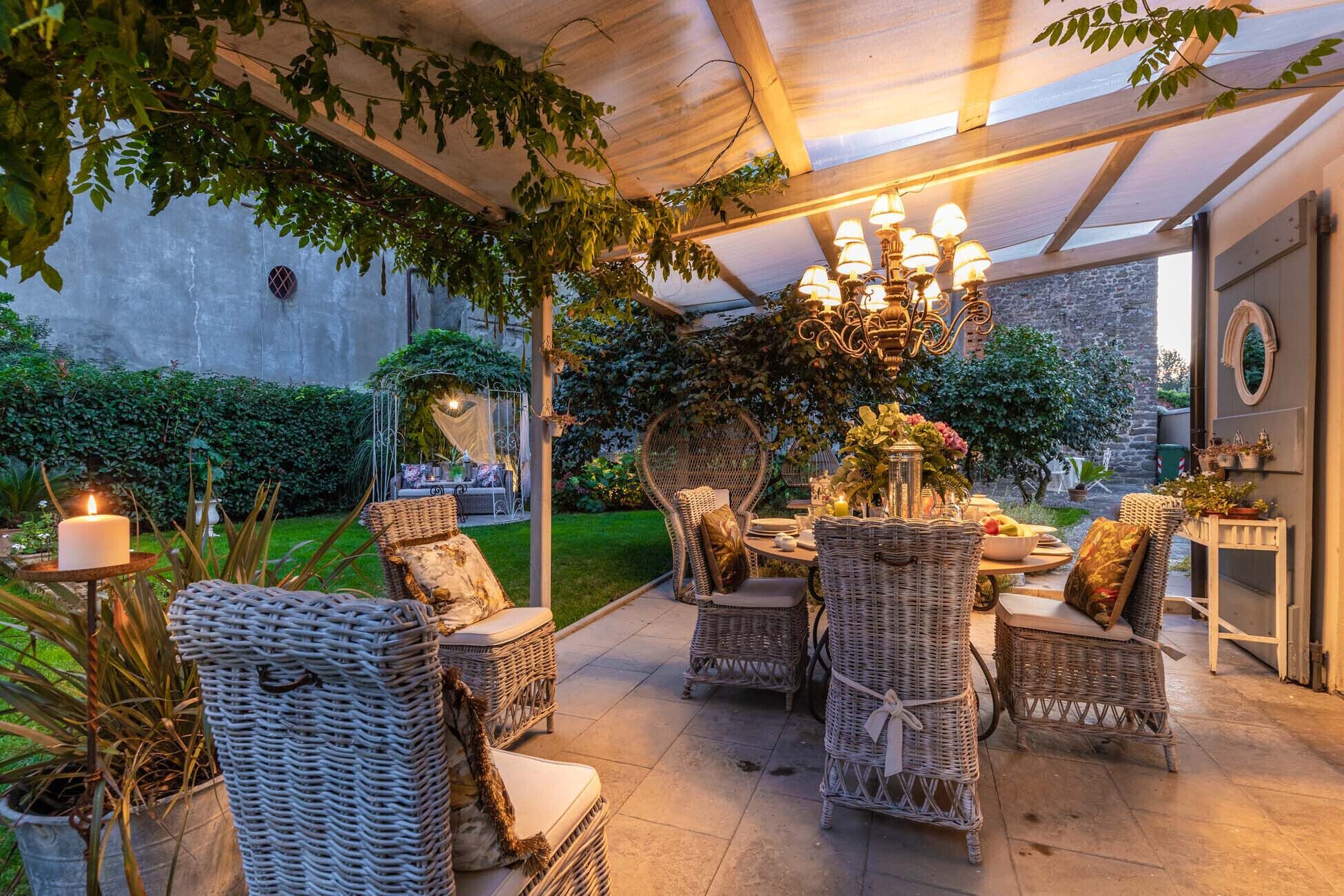 Un patio exterior con mobiliario de mimbre, una mesa dispuesta para comer y una lámpara decorativa.