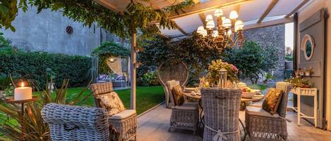 Un patio exterior con mobiliario de mimbre, una mesa dispuesta para comer y una lámpara decorativa.