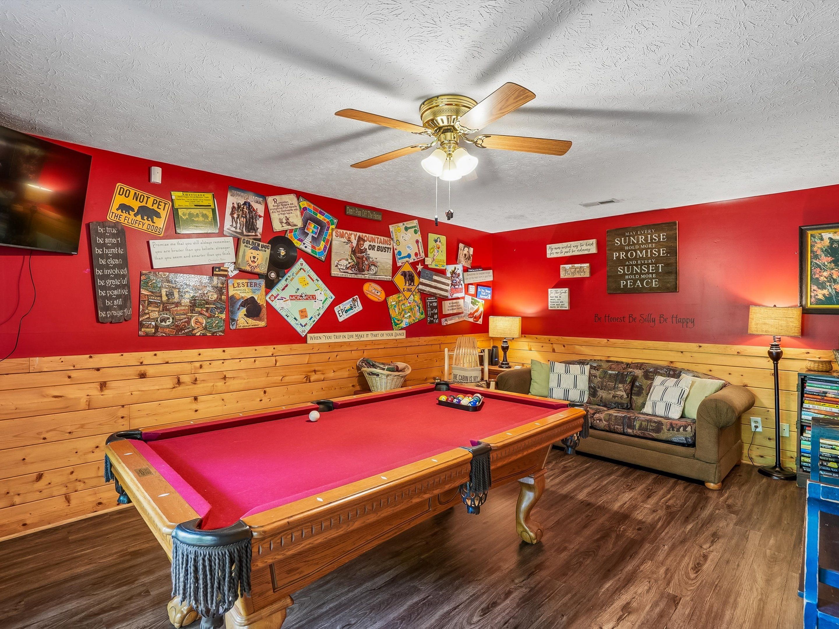 Une table de billard dans une pièce dont un mur rouge est décoré de divers affiches et panneaux.