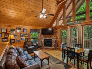 A cozy cabin interior with a fireplace, wooden walls, a sofa, a television, and a dining area. - Americana by Jackson Mountain Rentals (Gatlinburg)