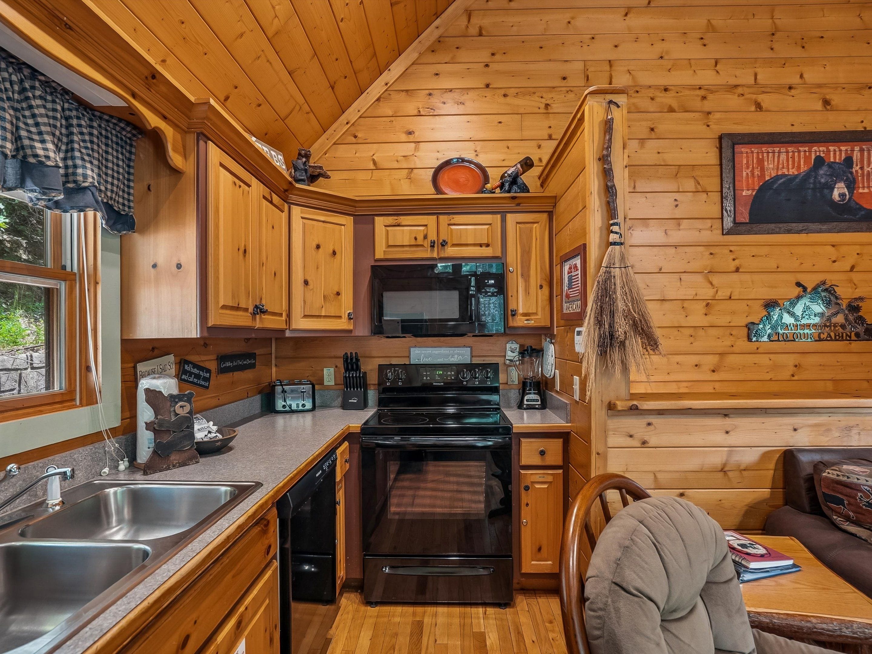 A cabin interior with wooden walls, a kitchen area including a stove, sink, and microwave, and a dining area with a table and chairs.
