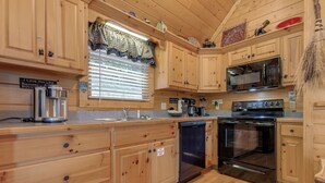 A kitchen with wooden cabinets, a microwave, an oven, a dishwasher, and a window with blinds. - Americana by Jackson Mountain Rentals (Gatlinburg)
