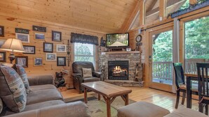 A cozy cabin interior with a fireplace, comfortable seating, and a television. - Americana by Jackson Mountain Rentals (Gatlinburg)